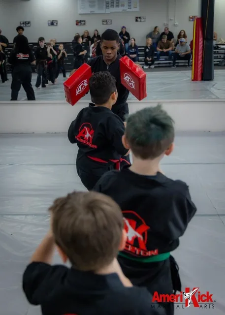Kids Martial Arts students lined up taking turns kicking pads held by instructor